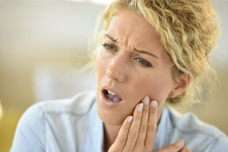 A blonde woman with curly hair has her hand to her jaw indicating tooth sensitivity.