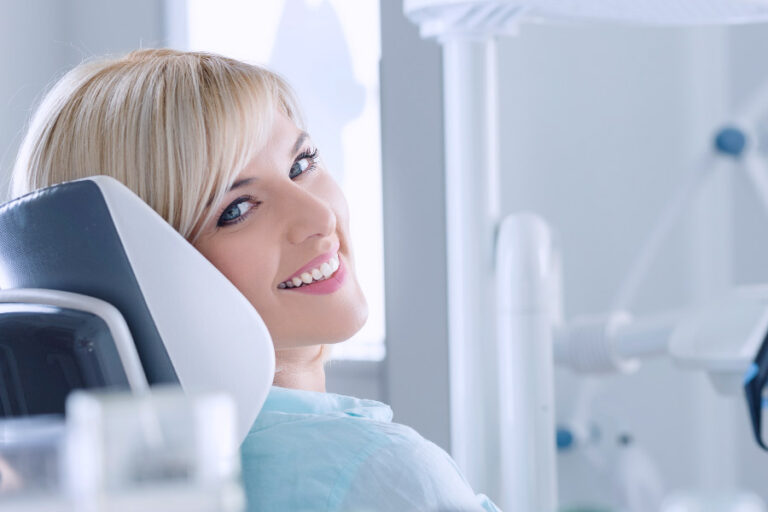 Smiling blonde woman with white teeth relaxing in the dental chair after teeth whitening treatment at Smiles Dental